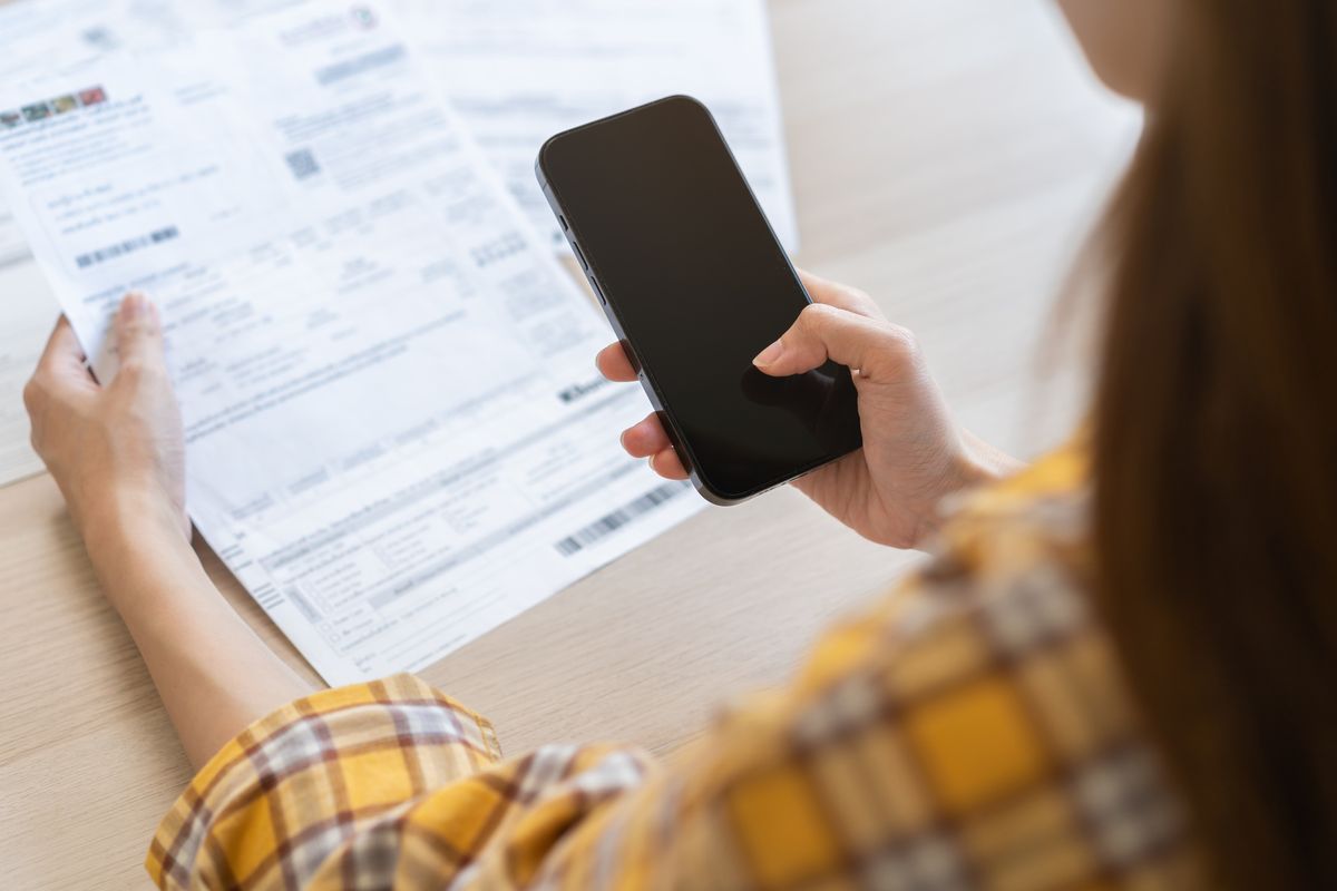 Persona revisa un documento con su celular en la mano