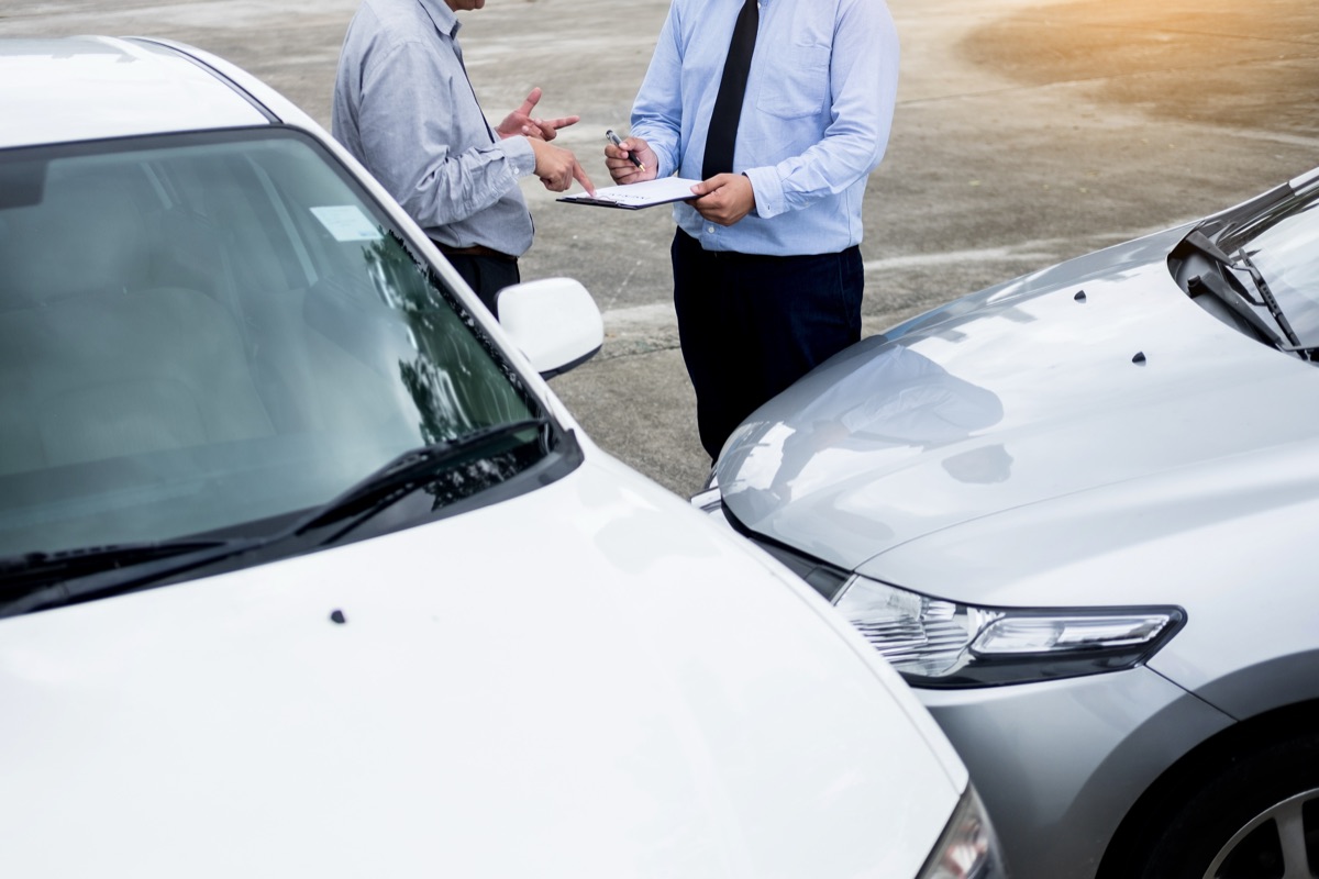 Ajustador y conductor revisan un documento entre dos autos chocados