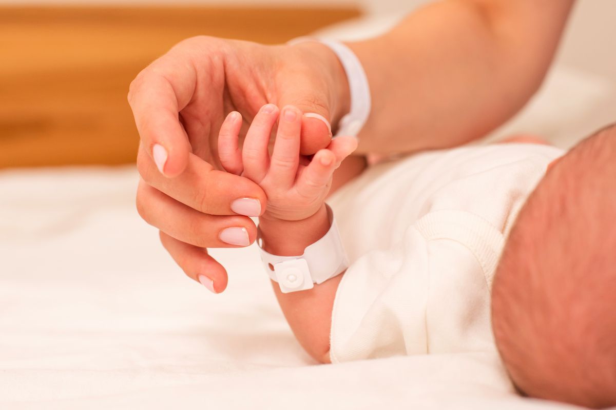 Mano de una mamá sosteniendo la mano de su bebé recién nacido con pulsera de hospital